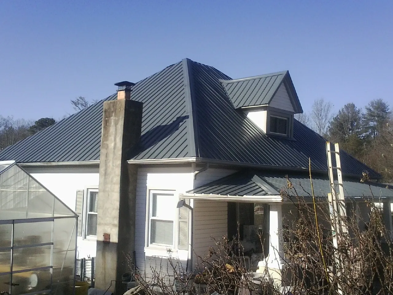 Dark blue standing seam metal roof on a white farmhouse with dormer — Slate & Tile Roof Repair by Roofing Brothers in Ozawkie