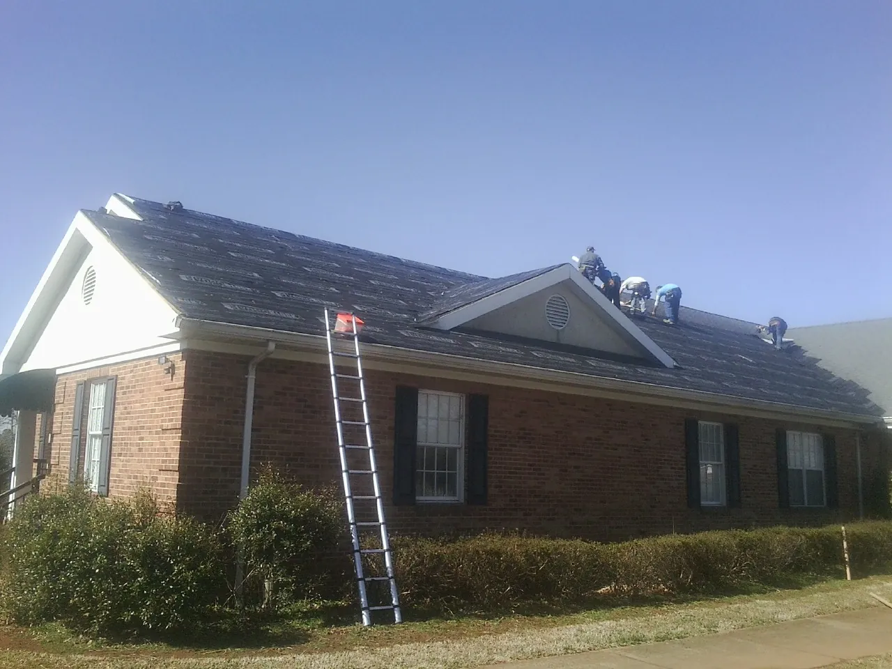 Crew tearing shingles off a brick ranch roof with a ladder set — Emergency Roof Repair work by our crew in Ozawkie