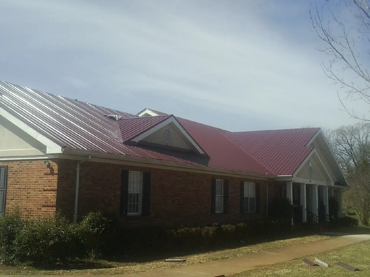 Red metal roof with gabled entries on a long brick building, from a Hail Damage Roof Repair job in Ozawkie