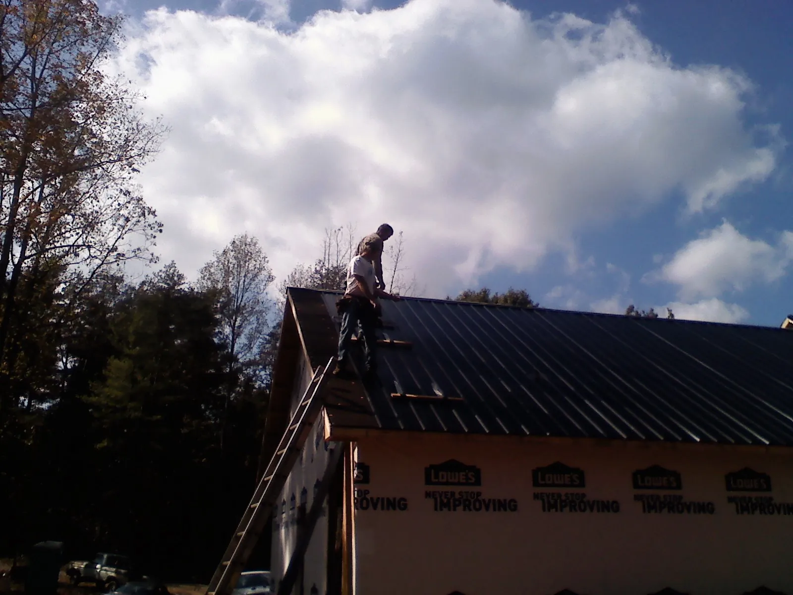 Roofer fastening dark metal panels high against a cloudy sky, from a Roof Inspection job in Ozawkie