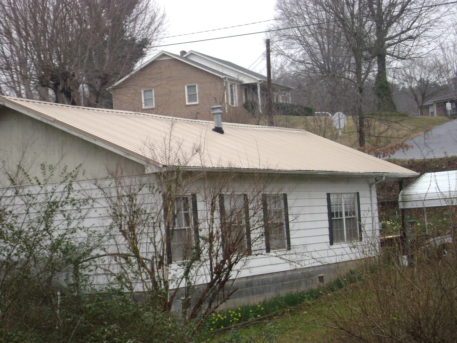 Tan metal roof on a white sided house set into a hillside — Commercial Roofing by Roofing Brothers in Ozawkie