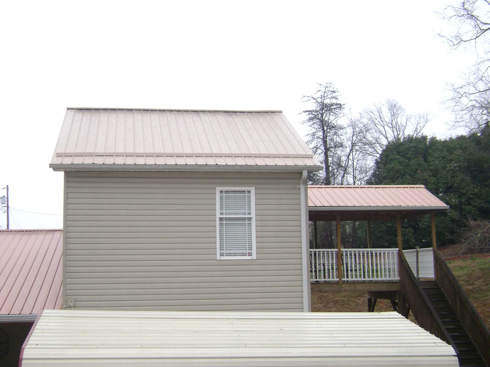 Tan metal roofs on a two story addition and attached porch, from a Roof Replacement job in Ozawkie